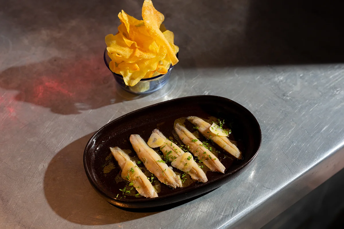 Brutalista, el restaurante de cocina española contemporánea liderado por Pablo López en el barrio madrileño de Argüelles, amplía su propuesta con una nueva franja horaria: desde esta temporada, abrirá de martes a viernes, de 18:00 a 21:00, en formato taberna. Una versión más informal y desenfadada que se articula en torno a una carta de tapas y raciones. La propuesta recupera algunos de los clásicos más reconocibles de la casa como la codorniz frita o la sardina ahumada, e incorpora nuevas propuestas como las patatas con alioli de sésamo y caballa, el montadito de pata frita o los boquerones en vinagre. También hay espacio para productos especialmente valorados, como la gamba de Huelva, siempre bajo la mirada de una cocina que reivindica el producto, la temporada y el sabor.