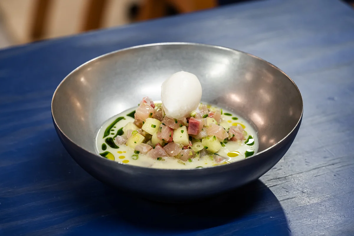 Krudo   En Krudo, la carta nunca permanece quieta. El raw bar de Rafa Bergamo, ubicado en el Mercado de Vallehermoso, da la bienvenida a la nueva temporada con una selección de platos que refuerzan su esencia: producto de mercado, técnica, brasas y una clara inspiración viajera. Las novedades recorren distintos rincones del mundo sin perder de vista el protagonismo del mar, con propuestas que van desde un tiradito de corvina y gambón con leche de tigre de ají amarillo ahumado hasta un tartar de hiramasa con litchi, coco y habanero o unas flautas de langostino crujiente que mezclan influencias mexicanas y asiáticas.       La gran incorporación al apartado de brasas es una lubina zarandeada adobada con chiles mexicanos y acompañada de un refrescante som tam de mango verde. Todo ello se suma a una propuesta que evoluciona constantemente según el producto disponible y que convierte cada visita en una experiencia diferente del que es uno de los puestos gastronómicos más interesantes de Vallehermoso.   