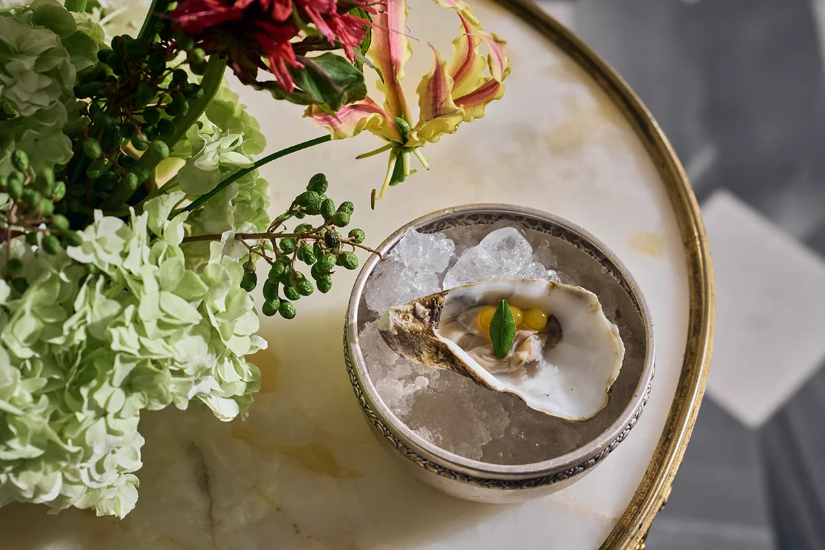 Relais & Châteaux Heritage Hotel eleva este icónico formato a su máxima expresión, demostrando que la alta gastronomía también se disfruta en formato de bocado, con el producto de proximidad y la técnica vanguardista unidos para dar forma a una experiencia gourmet. El chef Mario Sandoval ha diseñado una propuesta que rinde homenaje a los grandes clásicos de la cocina española con opciones ligeras que van desde las clásicas e imprescindibles gildas de anchoa con piparra encurtida o el jamón de bellota con D.O. Ibérico, hasta elevadas apuestas como la ostra con jalapeños y fruta de la pasión. No faltan las croquetas de jamón ibérico, el crujiente torrezno de papada ibérica o un clásico imprescindible de la capital: los tradicionales Soldaditos de Pavía en formato de buñuelos de bacalao. Como guiño a la gastronomía madrileña, su versión más cuidada de los tradicionales callos a la madrileña, las patatas bravas o una impecable tortilla española.
