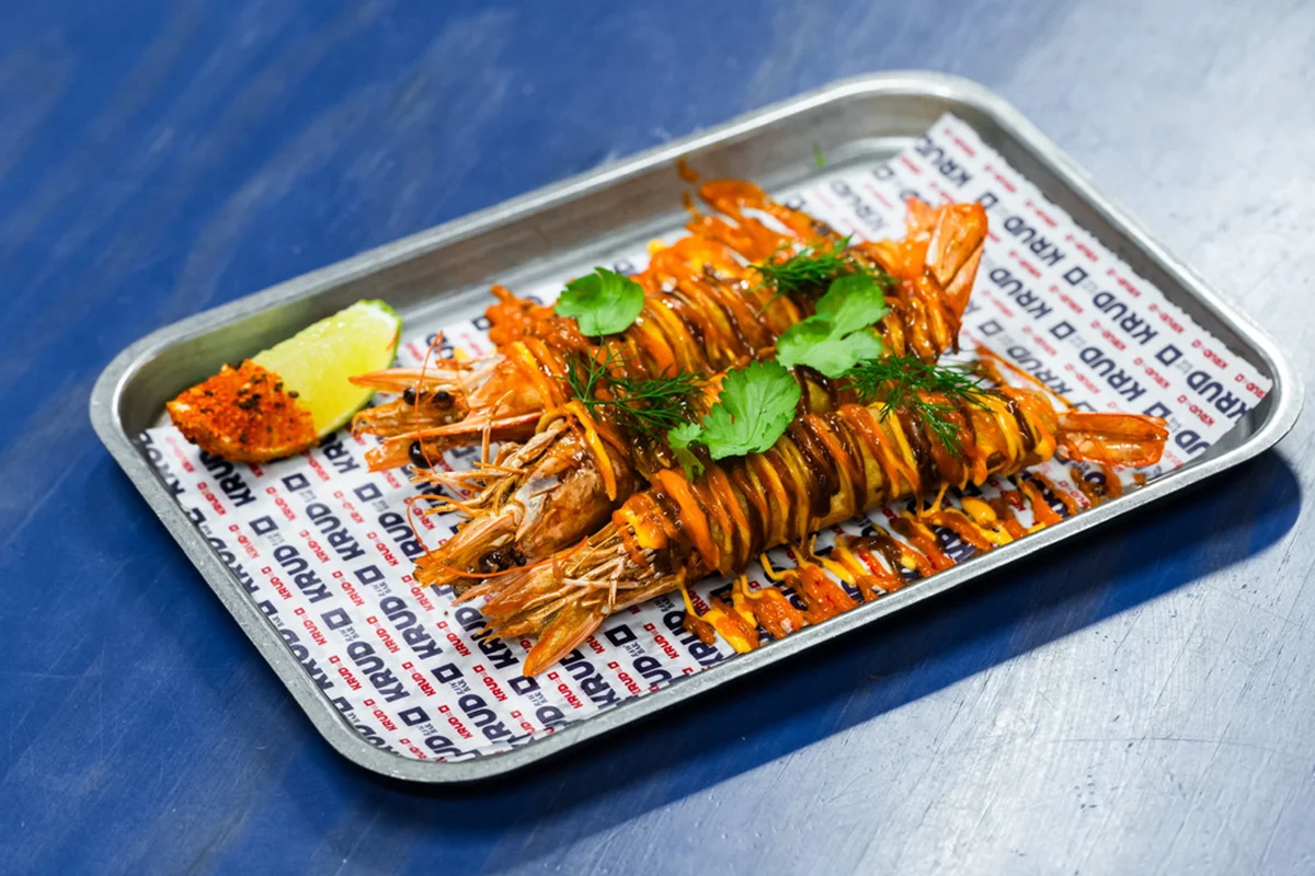 Krudo   En Krudo, la carta nunca permanece quieta. El raw bar de Rafa Bergamo, ubicado en el Mercado de Vallehermoso, da la bienvenida a la nueva temporada con una selección de platos que refuerzan su esencia: producto de mercado, técnica, brasas y una clara inspiración viajera. Las novedades recorren distintos rincones del mundo sin perder de vista el protagonismo del mar, con propuestas que van desde un tiradito de corvina y gambón con leche de tigre de ají amarillo ahumado hasta un tartar de hiramasa con litchi, coco y habanero o unas flautas de langostino crujiente que mezclan influencias mexicanas y asiáticas.       La gran incorporación al apartado de brasas es una lubina zarandeada adobada con chiles mexicanos y acompañada de un refrescante som tam de mango verde. Todo ello se suma a una propuesta que evoluciona constantemente según el producto disponible y que convierte cada visita en una experiencia diferente del que es uno de los puestos gastronómicos más interesantes de Vallehermoso.   
