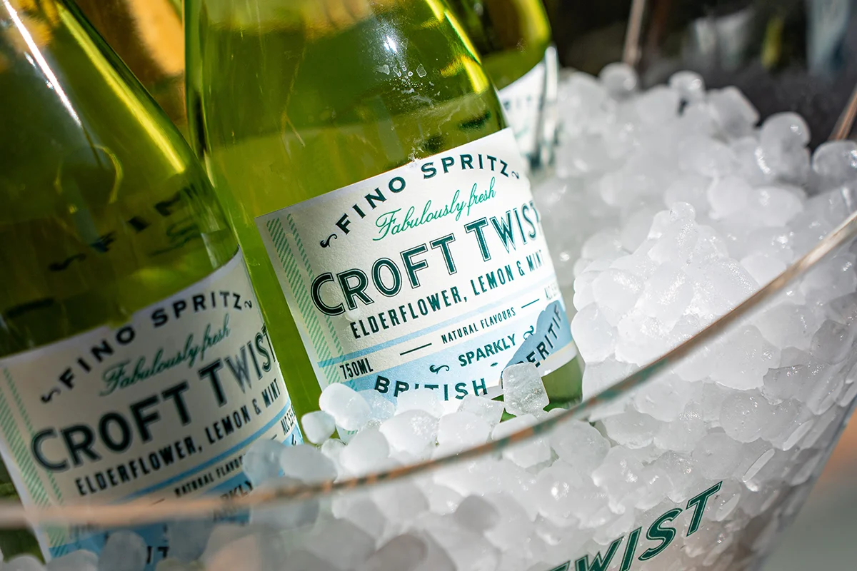 CROFT TWIST    El spritz ya no habla solo italiano, sino que ahora tiene acento andaluz. Croft Twist es una propuesta que cambia el prosecco por vino fino y convierte el aperitivo en algo más fresco, ligero y sorprendente. Con una graduación de apenas 5,5º, esta bebida se ha ganado un hueco entre quienes buscan alternativas más suaves sin renunciar al sabor ni al ritual de la copa al atardecer.      Su fórmula mezcla finos elegantes elaborados en las bodegas centenarias de González Byass con ingredientes naturales como hierbabuena y limón, dando lugar a un perfil cítrico, delicado y muy fácil de beber. La burbuja es fina, ligera y pensada para acompañar esos tardeos interminables que empiezan sin saber cuándo terminan. Croft Twist representa una nueva generación de aperitivos: menos intensos, más espontáneos y ligados a momentos sociales diurnos donde importa tanto la bebida como el ambiente que la rodea.   