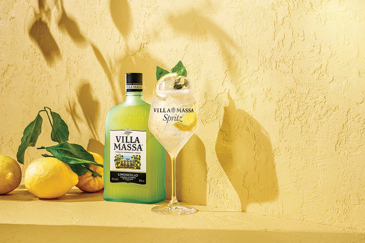 VILLA MASSA    ¿Y qué es el verano sin frutas cítricas? Villa Massa parte de estas para reinterpretar el clásico spritz con una propuesta muy sorrentina, donde el limoncello se convierte en protagonista absoluto. El resultado es Villa Massa Spritz, un cóctel fresco, cítrico y luminoso que transforma el aperitivo en algo mucho más relajado y mediterráneo. La receta combina la intensidad dulce y natural del limoncello, elaborado con los excepcionales limones de Sorrento, la burbuja sofisticada del Prosecco y un toque de soda que equilibra el conjunto.      Fácil de beber y pensado para alargar sobremesas, tardes infinitas o cenas al aire libre, este spritz se mueve entre la tradición italiana y una nueva generación de cócteles más ligeros y versátiles. Servido con hielo, rodajas de limón y hojas de albahaca, cada copa se siente como un aperitivo elegante, sencillo y refrescante que entiende perfectamente a qué sabe el verano. 