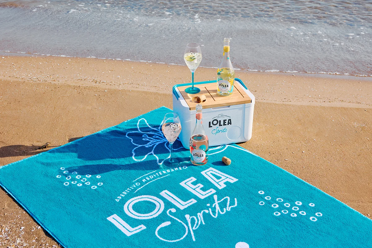 LOLEA    Lolea entra en este universo con una propuesta que apuesta por sabores mediterráneos, ingredientes naturales y una estética tan cuidada como la propia bebida. Su gama Lolea Spritz nace alrededor de dos versiones muy distintas, pero igual de apetecibles: Citrus Spritz y Floral Spritz. La primera combina vino blanco espumoso con notas de bergamota, cítricos y un toque aromático de albahaca que la hace especialmente fresca y ligera. La segunda se mueve en un terreno más suave y floral, mezclando vino rosado, naranja sanguina y azahar en una combinación delicada y ligeramente ácida que funciona especialmente bien al atardecer. Ambas referencias tienen una graduación moderada del 8% y están elaboradas mediante el método Charmat, responsable de esa burbuja fina y elegante que hace que cada sorbo resulte más suave.  