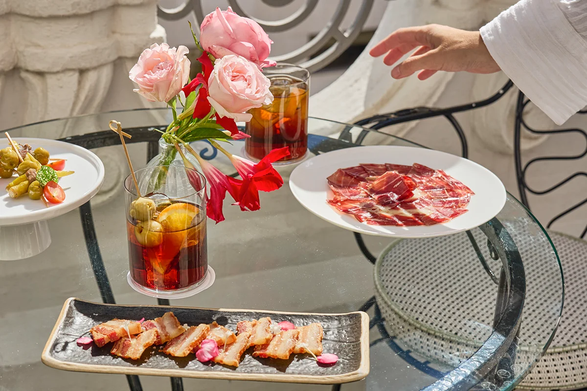 Relais & Châteaux Heritage Hotel eleva este icónico formato a su máxima expresión, demostrando que la alta gastronomía también se disfruta en formato de bocado, con el producto de proximidad y la técnica vanguardista unidos para dar forma a una experiencia gourmet. El chef Mario Sandoval ha diseñado una propuesta que rinde homenaje a los grandes clásicos de la cocina española con opciones ligeras que van desde las clásicas e imprescindibles gildas de anchoa con piparra encurtida o el jamón de bellota con D.O. Ibérico, hasta elevadas apuestas como la ostra con jalapeños y fruta de la pasión. No faltan las croquetas de jamón ibérico, el crujiente torrezno de papada ibérica o un clásico imprescindible de la capital: los tradicionales Soldaditos de Pavía en formato de buñuelos de bacalao. Como guiño a la gastronomía madrileña, su versión más cuidada de los tradicionales callos a la madrileña, las patatas bravas o una impecable tortilla española.
