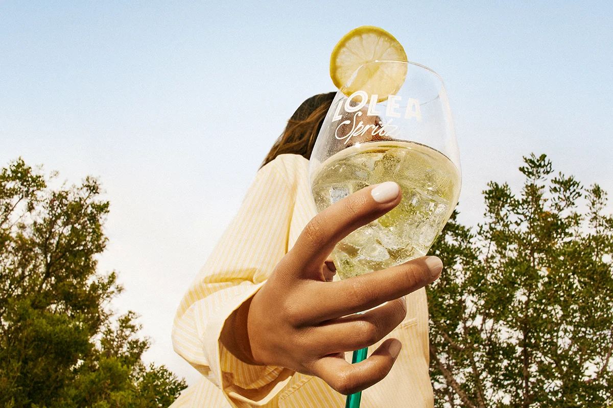 LOLEA    Lolea entra en este universo con una propuesta que apuesta por sabores mediterráneos, ingredientes naturales y una estética tan cuidada como la propia bebida. Su gama Lolea Spritz nace alrededor de dos versiones muy distintas, pero igual de apetecibles: Citrus Spritz y Floral Spritz. La primera combina vino blanco espumoso con notas de bergamota, cítricos y un toque aromático de albahaca que la hace especialmente fresca y ligera. La segunda se mueve en un terreno más suave y floral, mezclando vino rosado, naranja sanguina y azahar en una combinación delicada y ligeramente ácida que funciona especialmente bien al atardecer. Ambas referencias tienen una graduación moderada del 8% y están elaboradas mediante el método Charmat, responsable de esa burbuja fina y elegante que hace que cada sorbo resulte más suave.  