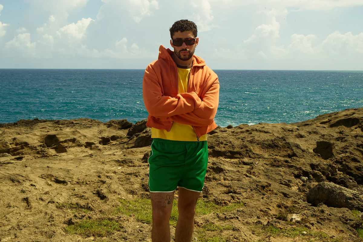 “Un verano en NUEVAYoL”… con Benito aterrizando en España. Coincidiendo con el arranque de sus conciertos en España, la marca de Inditex lanza BENITO ANTONIO, una cápsula de casi 150 piezas que traduce el universo estético del artista puertorriqueño a prendas pensadas para el día a día. Oversize, sastrería relajada, camisetas gráficas, bermudas amplias, bandanas y tejidos ligeros forman parte de una propuesta que bebe directamente de Puerto Rico y de esa manera despreocupada —pero muy medida— de vestir que define a Benito. Lejos de parecer el típico merchandising de gira, la colección funciona como una extensión real de su estilo personal: colores vibrantes, siluetas cómodas y ese punto entre urbano y nostálgico que domina también sus últimos trabajos musicales. Además, llega en uno de los momentos de mayor locura, con fans agotando prendas en cuestión de horas y preparando looks para los conciertos de Madrid y Barcelona.