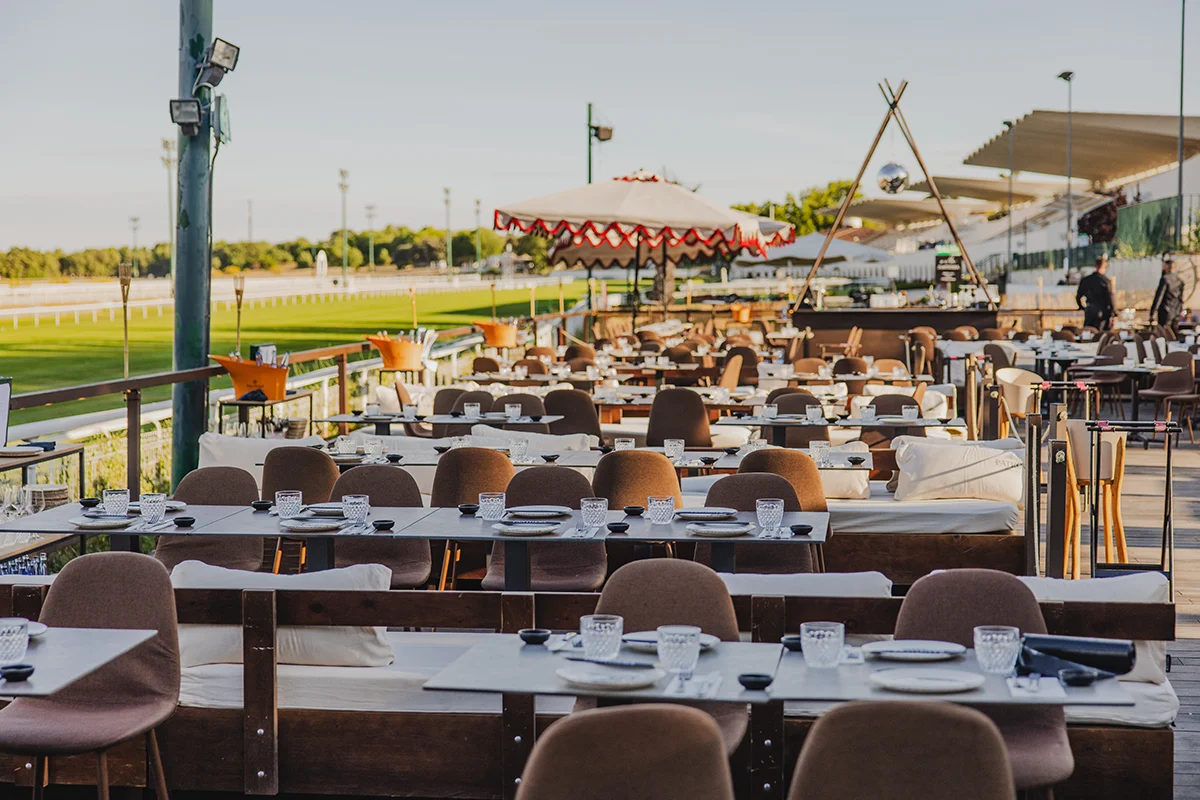 Villa Panthera   Madrid en verano tiene una categoría propia de planes, entre los que se encuentran aquellos que se quedan en la memoria, como pasa con Villa Panthera. Instalado en el Hipódromo de la Zarzuela, este formato vuelve a convertir uno de los enclaves más icónicos de la ciudad en escenario de noche larga, donde el atardecer marca el inicio y la música el ritmo de lo que viene después. El entorno lo pone el propio Hipódromo, con sus vistas abiertas a la pista y esa sensación de amplitud que difícilmente se encuentra dentro de la M-30; la puesta en escena la firma Panthera, con una mezcla de gastronomía, coctelería y ambiente que va creciendo a medida que avanza la noche. La propuesta gastronómica está pensada para compartir y alargar la experiencia, con platos como ostras con ponzu y caviar cítrico, ceviches, tiraditos, sushi elaborado al momento o guiños más contundentes como el katsu sando o la smashburger de txuleta. Todo se acompaña de una carta líquida cuidada y una música que, lejos de ser decorado, forma parte del propio relato.