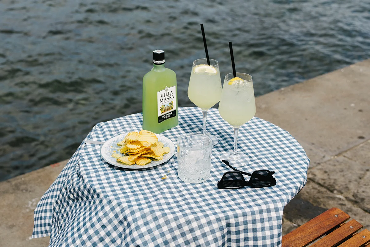 VILLA MASSA    ¿Y qué es el verano sin frutas cítricas? Villa Massa parte de estas para reinterpretar el clásico spritz con una propuesta muy sorrentina, donde el limoncello se convierte en protagonista absoluto. El resultado es Villa Massa Spritz, un cóctel fresco, cítrico y luminoso que transforma el aperitivo en algo mucho más relajado y mediterráneo. La receta combina la intensidad dulce y natural del limoncello, elaborado con los excepcionales limones de Sorrento, la burbuja sofisticada del Prosecco y un toque de soda que equilibra el conjunto.      Fácil de beber y pensado para alargar sobremesas, tardes infinitas o cenas al aire libre, este spritz se mueve entre la tradición italiana y una nueva generación de cócteles más ligeros y versátiles. Servido con hielo, rodajas de limón y hojas de albahaca, cada copa se siente como un aperitivo elegante, sencillo y refrescante que entiende perfectamente a qué sabe el verano. 