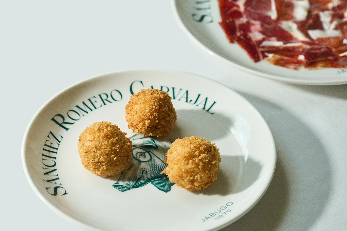 Ruta de la Croqueta de Sánchez Romero Carvajal La croqueta es uno de esos clásicos siempre presente en los mejores momentos de tapeo y terraceo. Los amantes de esta elaboración están de enhorabuena porque ya pueden disfrutar de la Ruta de la Croqueta de Sánchez Romero Carvajal, celebración que cumple su cuarta edición con una propuesta más amplia y con más fuerza que nunca. Hasta el 6 de julio, este recorrido se instala como una de las citas gastronómicas más esperadas del inicio del verano con los nuevos participantes como Salino, Los Gabrieles, Árdia, Rita Sibarita, Casa Vega, Cachivache (Serrano), La Raquetista, Cachivache (Montecarmelo) y El Gallego, que amplían el itinerario con nuevas interpretaciones de este clásico. Las incorporaciones se suman a algunos de los grandes nombres de otras ediciones como Casa Orellana, Tatel, Casa Salesas, Café Comercial, 11 Nudos, El Escondite de Villanueva o Virrey. Además, con motivo del Día Mundial de la Tapa, la ruta amplía su propuesta con una irresistible selección de tapas elaboradas con jamón ibérico.