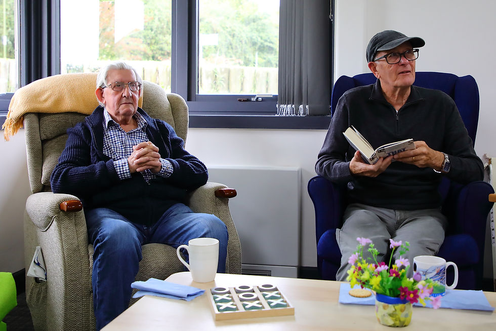 Two men living with dementia sat in comfortable chairs at Sage House respite care.
