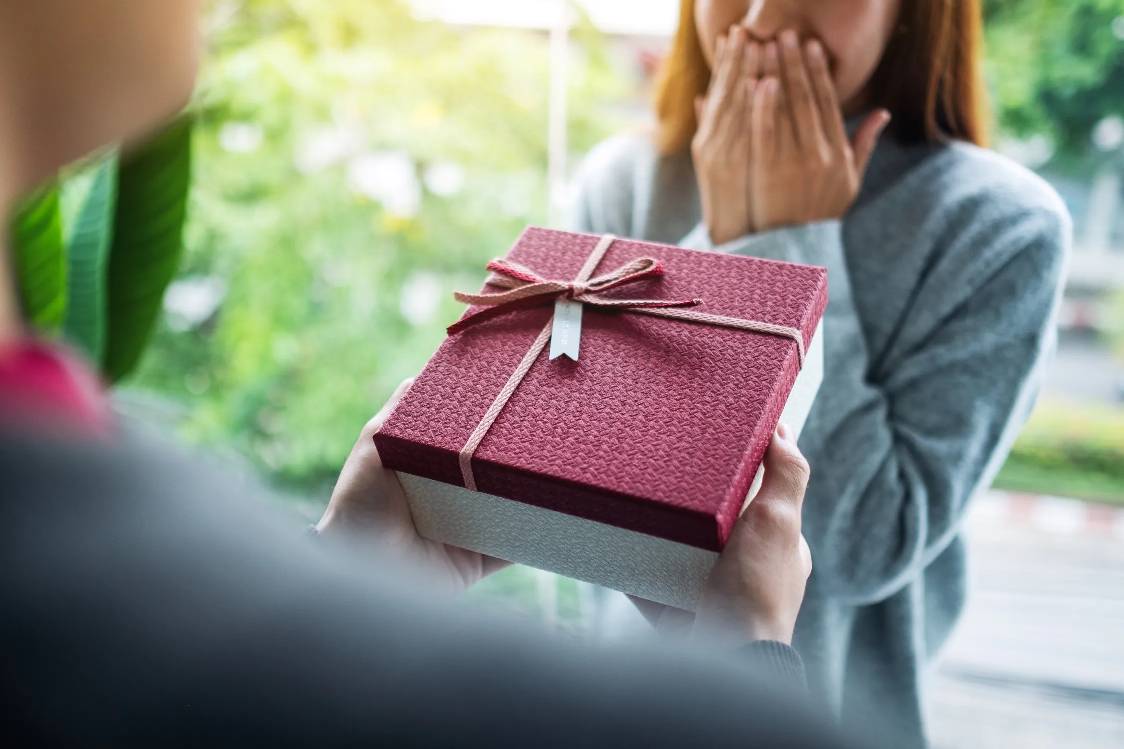 Man gifting a special gift in a red box with bow to a woman who is thankful for a thoughtful give on their couple anniversay