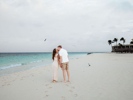 Pregnant couple walking hand in hand on the beach in Aruba, showing off baby bump during romantic maternity photoshoot.