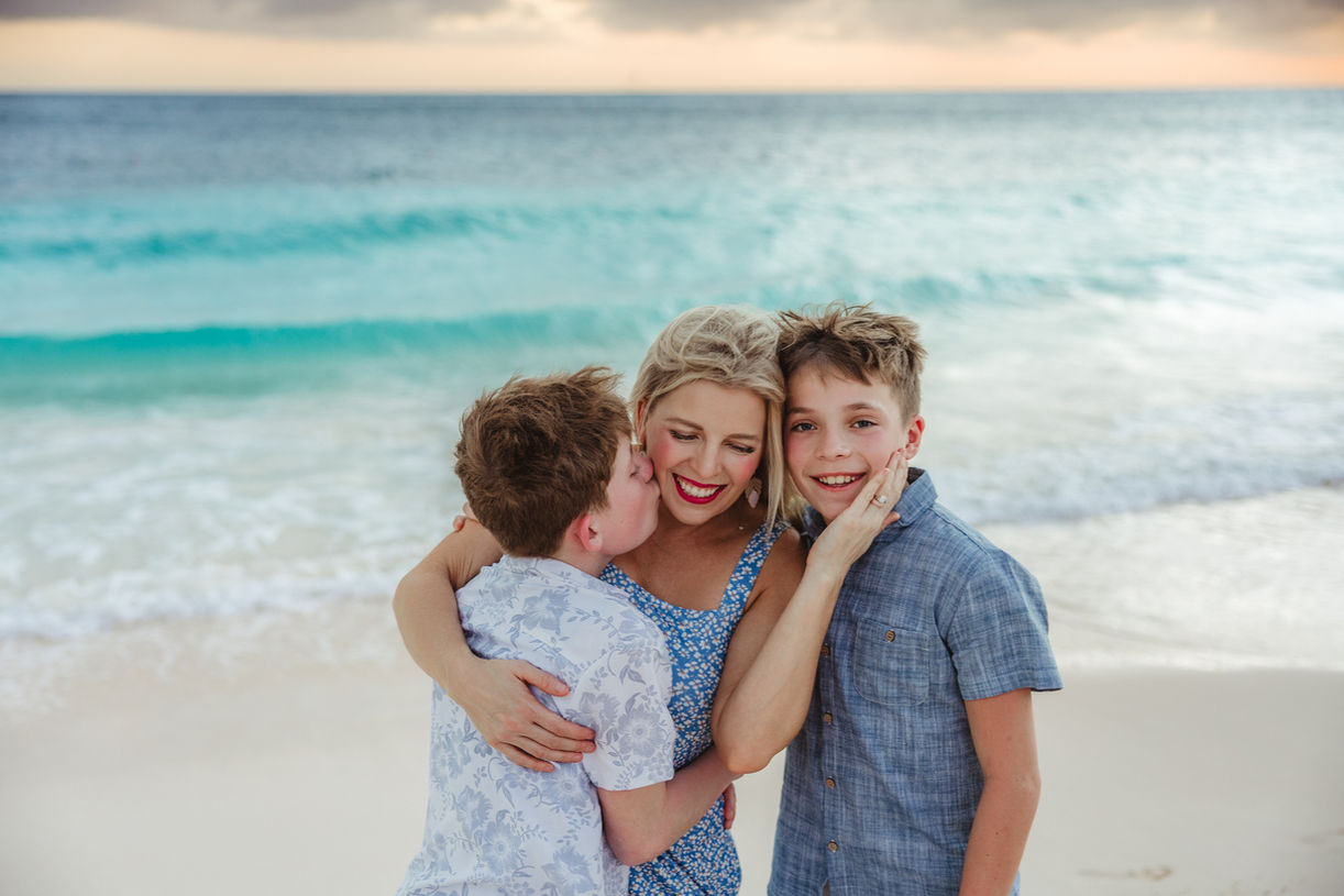 Mother being kissed by her kids during a photo session in Aruba on the beach wearing blue outfits