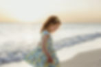 Girl in a floral dress walking on a beach at sunset, with gentle waves and a serene expression.