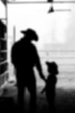 a black and white silhouette of a father and son standing in a barn. Father looking down at son.