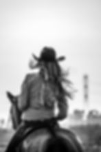Cowgirl in a hat on horseback, viewed from behind