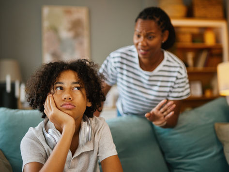 African American mother scolding teenage her son at home on green couch