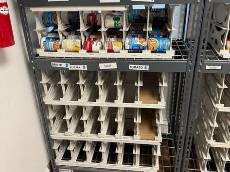Metal pantry shelf with labeled soup bins and mostly empty slots, a few canned soups on the top shelf.