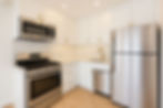Bright white modern kitchen with stainless steel fridge, microwave and stove, gold hardware, herringbone backsplash, and empty counters