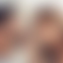 Couple lying on white bed, smiling at each other. The woman playfully touches the man's nose. Bright, warm lighting enhances the cozy mood.