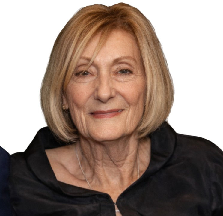 An older woman with short blonde hair smiles softly, wearing a black top against a white background, conveying a calm and pleasant mood.
