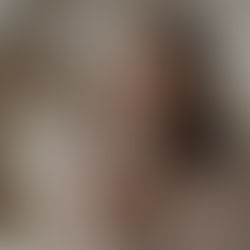 Woman in a beige sweater holding a white mug, eyes closed, smiling in contentment. Soft, neutral background suggests a cozy setting.