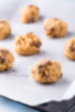 Chocolate chip cookie dough balls on baking sheet with parchment paper, ready to bake. Warm, inviting kitchen setting.