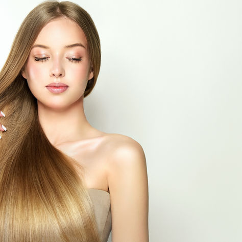 Woman with long straight hair gently holds her hair, eyes closed, against a plain white background, serene portrait.