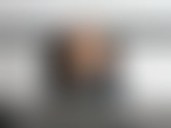 Woman in dark jacket sits at desk with laptop, covering face with hands, showing frustration. Calculator and pen on table, whiteboard behind.