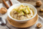 Bowl of Maple Walnut Oatmeal by Stacey Antine, MS, RD, topped with sliced green apples and cinnamon. Surrounded by walnuts, a cinnamon stick, and a spoon on a wooden table. Bergen County Moms.