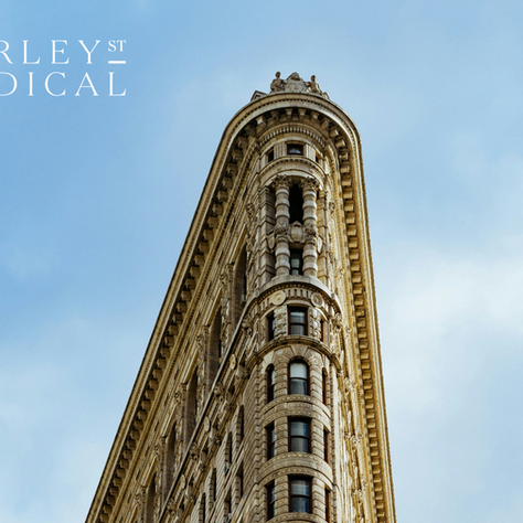 Harley St Medical text over a low-angle view of a narrow ornate stone building against a blue sky.
