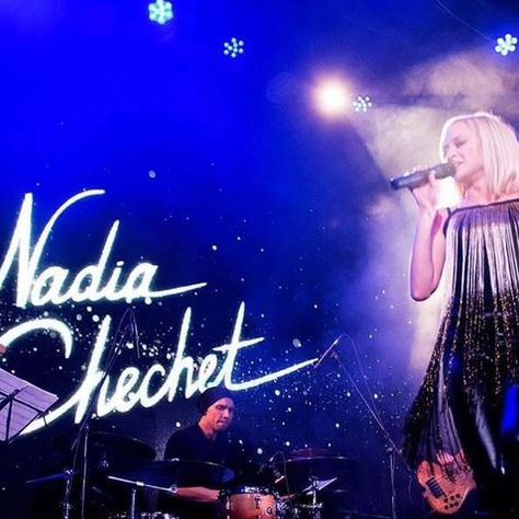 Singer performs on stage with blue lights, holding a microphone. "Nadia Chechet" text is visible. Drummer plays in the background. Energetic mood.
