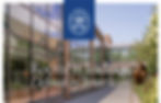 School building with glass windows, green trees, and a blue sky. White text reads "Rooted in Tradition. Defined by Innovation."