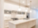 Bright modern white kitchen with marble island, gold pendant lights, stainless appliances, and sleek cabinets, no people.