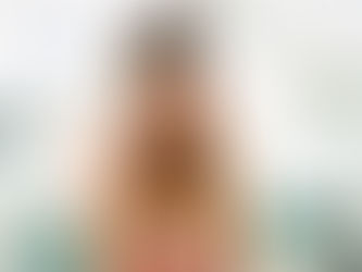 Woman in a striped shirt holds her head in pain, appearing stressed in a living room with green pillows and blurred decor in the background.