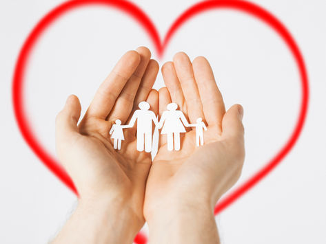 Hands hold paper cutouts of a family against a white background with a red heart outline, symbolizing love and protection.