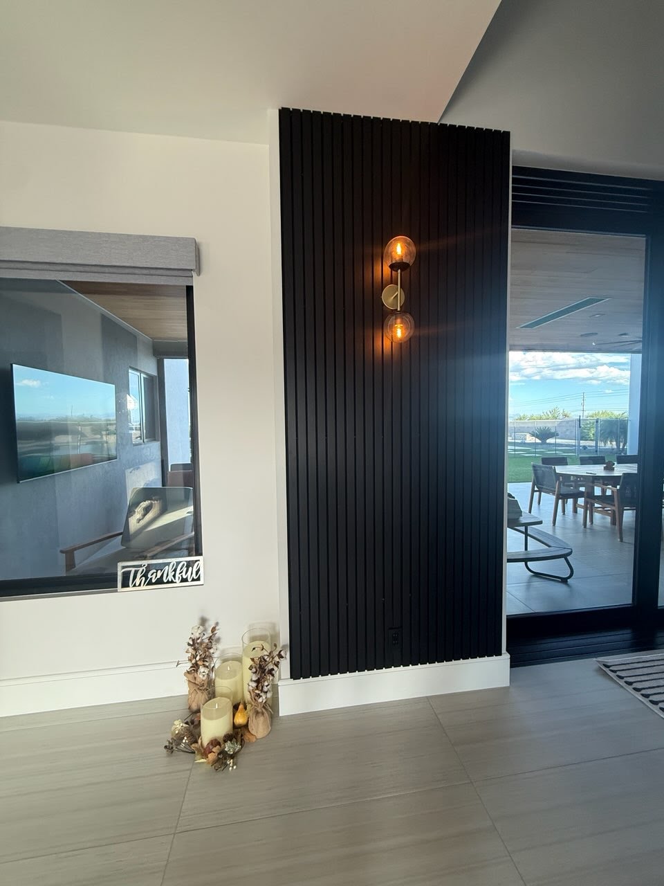 Black acoustic slat wood wall panels installed on a tall hallway feature wall with a warm decorative wall sconce