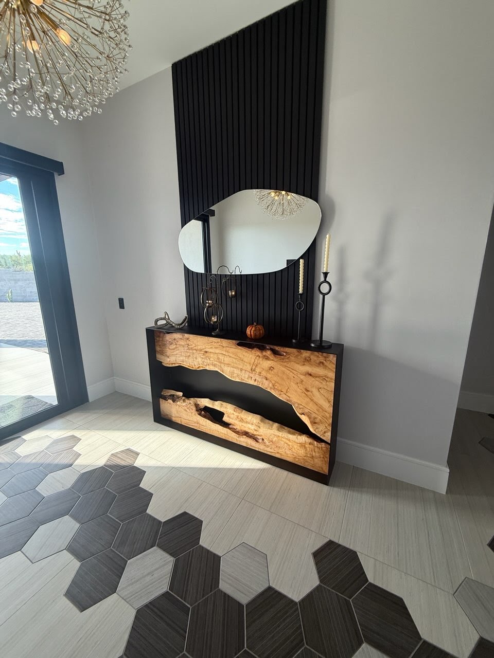 Black acoustic slat wood wall panels on an entryway accent wall above a natural wood console and mirror