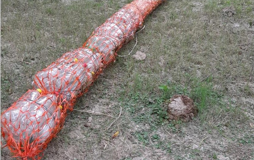 Detalle de una biobarda de botellas y malla naranja extendida sobre el suelo
