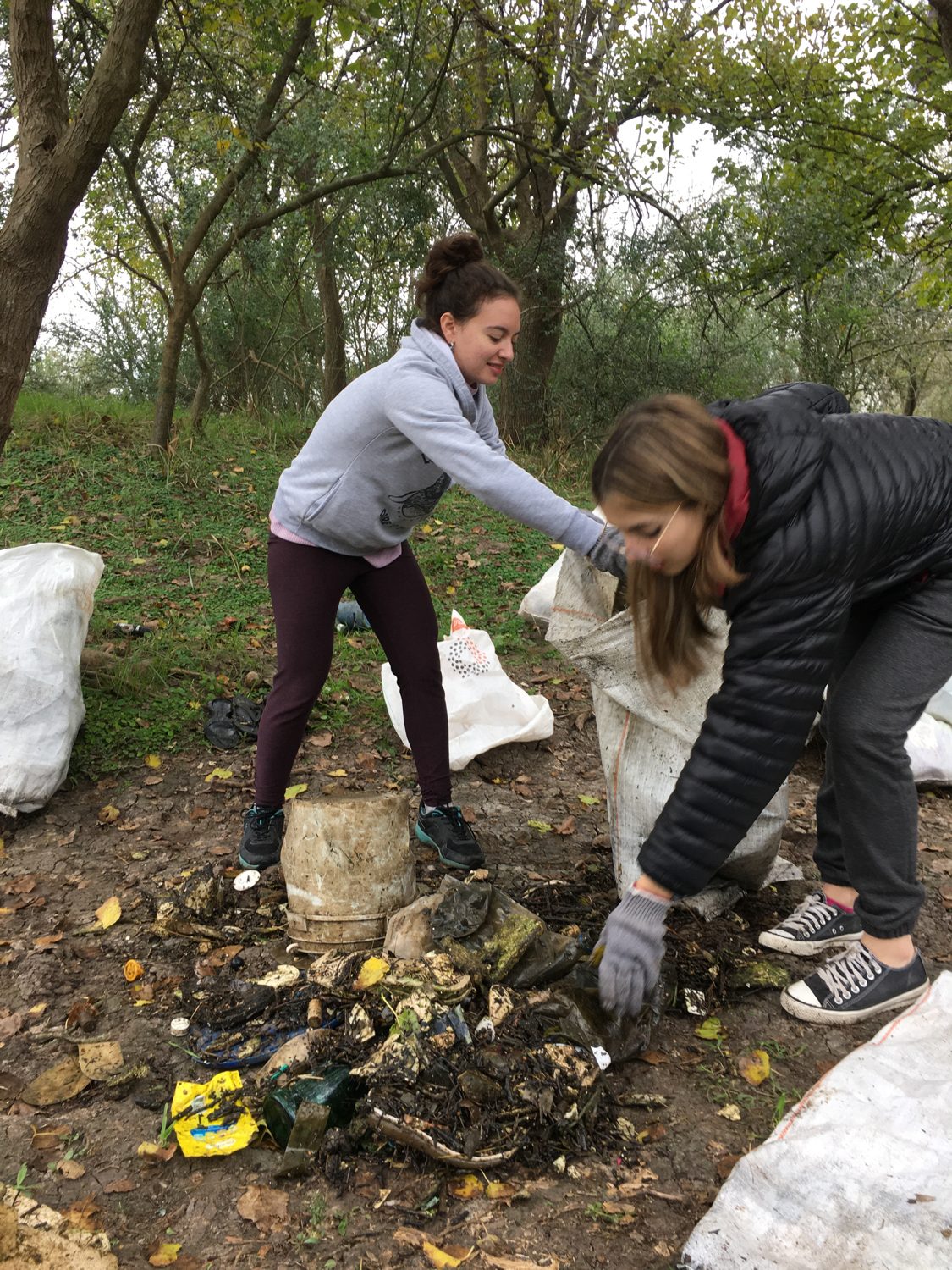 Dos voluntarias con guantes recolectando residuos entre la vegetación ribereña
