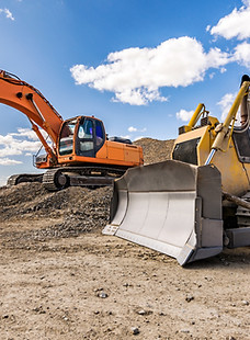 A yellow bulldozer and orange excavator parked next to one another on a dirt road under a blue sky
