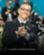 Central Cee in black suit smiles, pointing a camera stick; blue and floral background, cheerful mood. Text: Central Cee in Chrome Hearts.