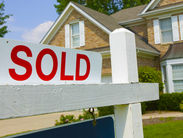 Sold sign in front of a suburban brick house with green lawn and trees. Bright day with clear sky, conveying a sense of accomplishment.