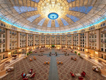 Grand hotel atrium with a glass domed ceiling, patterned carpet, and guests relaxing on chairs and sofas in a warm, elegant lobby