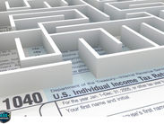 A 3D white maze sits atop a U.S. 1040 tax form, symbolizing complexity and confusion. The text is partially visible, adding to the challenge.