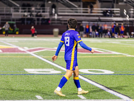 Westchester SC player Josh Drack wearing number 19 walks near midfield in blue home kit during a night match