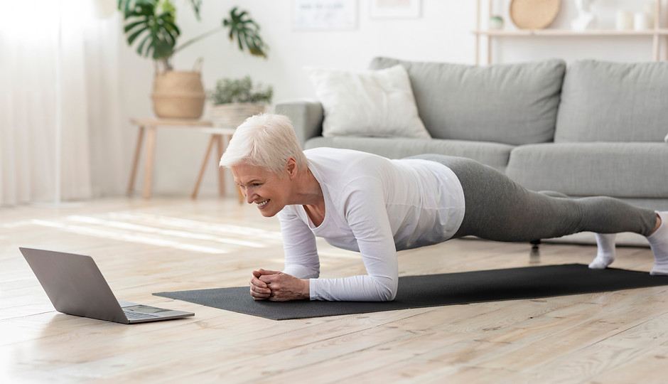 Training At Home. Sporty senior woman doing yoga plank while watching online tutorial on l