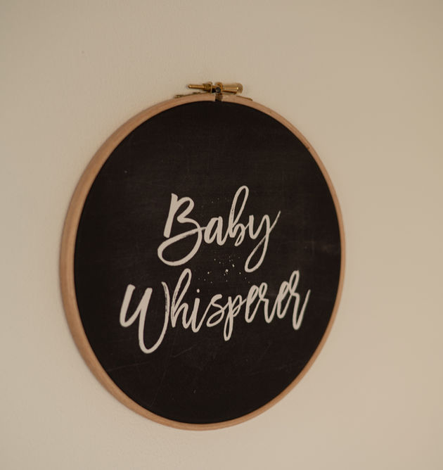 Runder, schwarzer Rahmen mit weißem Text Baby Whisperer an einer Wand.