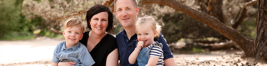 Familie sitzt zusammen und lächelt in die Kamera. FAMILIEN FOTOSHOOTING unter Baum