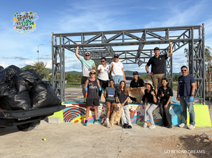Smiling volunteers pose under a steel frame by trash bags, with two dogs.